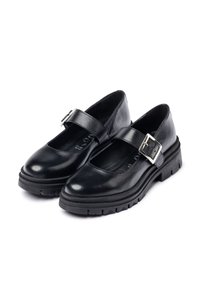 Zapatos Mary Jane de cuero negro con punta redonda, suela de goma gruesa y una correa ancha asegurada por una hebilla plateada. Textura suave, diseño minimalista.