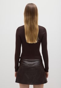 Maglione marrone a coste con maniche lunghe abbinato a una minigonna di pelle marrone con una texture liscia e cuciture visibili sul retro.