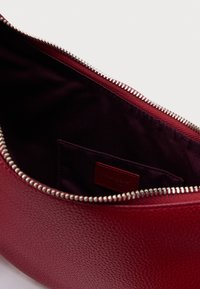Piros, texturált bőr táska belső része sötét szövet béléssel, ezüst cipzárral és egy kis belső zsebbel, amelyen márkajelzés található.