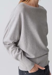 Jasnoszary sweter wykonany z miękkiego materiału, o luźnym kroju, z dekoltem typu łódka i prążkowanymi mankietami. Projekt obejmuje lekko zakrzywiony dół.