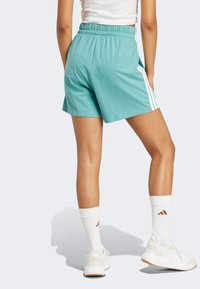 Teal urheilusortsit, joissa on joustava vyötärö, valkoiset sivupitkät ja sivutaskut; yhdistetty valkoisiin tennareihin ja nilkkasukkien kanssa.