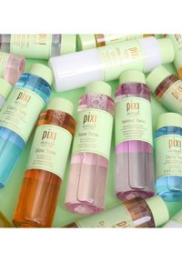 Tonici per la pelle Pixi assortiti in bottiglie cilindriche con liquidi colorati: blu, rosa, arancione e viola, ciascuno etichettato con informazioni sul prodotto.