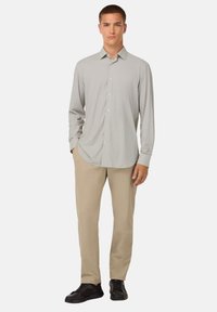 Camicia grigia chiaro a maniche lunghe con colletto a bottone e motivo sottile, abbinata a pantaloni beige e sneaker nere.
