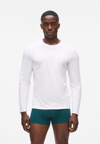 Hosszú ujjú fehér ing sima anyagból, zöld boxer nadrággal párosítva. Slim fit kialakítás, kerek nyakkivágással. Egyszerű és minimalista stílus.