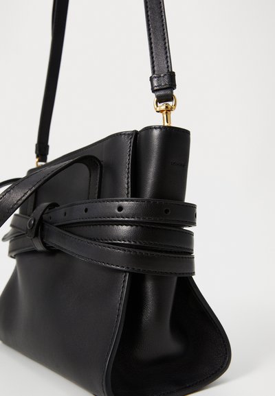 Sac à main en cuir noir avec une forme structurée, doté d'une bandoulière enveloppante, d'une texture lisse et d'une finition mate avec des accents en métal doré.
