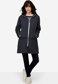 Laivastonsininen pilkullinen sadetakki, jossa on vetoketjukiinnitys, huppu ja kaksi sivutaskua. Valmistettu vesitiivistä materiaalia. Yhdistetty tummiin farkkuihin ja valkoisiin lenkkareihin.