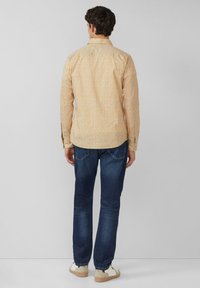 Lange mouwen, lichtoranje shirt met een klein bloemenpatroon, gecombineerd met een blauwe spijkerbroek en witte sneakers. Achteraanzicht toont het ontwerp van het shirt.