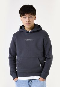 Sudadera gris oscuro con bolsillo frontal, capucha con cordón y texto blanco que dice "OBJETIVOS FUTUROS PERSPECTIVA FRESCA". Corte relajado, textura suave.