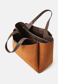 Bruine leren tote bag van suede met donkerbruine leren handvatten en interieur, voorzien van een geordend binnenvak met rits en een magnetische drukknoopsluiting.