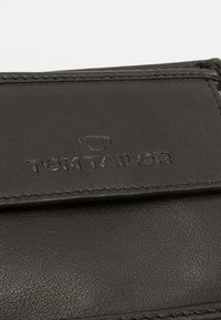 Portefeuille en cuir noir avec le logo "TOM TAILOR" en relief, avec des détails de couture le long des bords. Texture lisse et design compact.