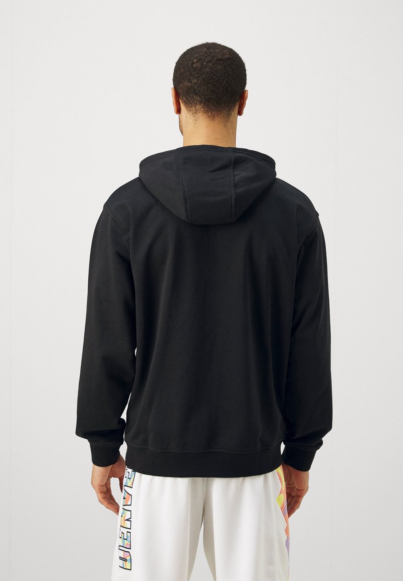 Sudadera con capucha negra de manga larga, hecha de una tela suave, con un corte relajado y un diseño sencillo. Costuras visibles a lo largo de los bordes.