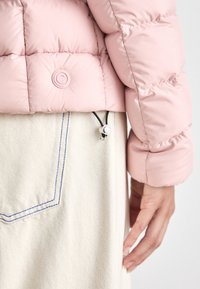 Απαλή ροζ φουσκωτή ζακέτα με κυκλικό κουμπί λογότυπο, διαθέτει κορδόνι και ασημί αξεσουάρ. Συνδυάζεται με μία ανοιχτόχρωμη υφασμάτινη φο�ύστα.