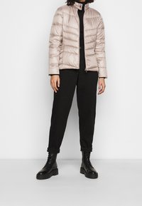 Světlý béžový prošívaný kabát s vysokým límcem, s horizontálním prošíváním. Kombinováno s černými kalhotami a černými šněrovacími vojenskými botami.