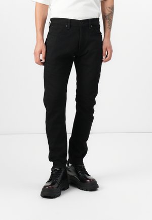 Black stretch denim pants with a slim fit; features five pockets, belt loops, and a mid-rise waist, paired with chunky black boots.