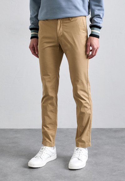 Pantalons khaki avec une coupe slim, en tissu de coton lisse, dotés d'une poche avant et d'une jambe fuselée, associés à des baskets blanches.