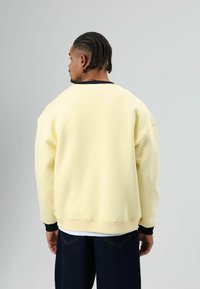 Fleece sweater in zacht geel, met een geribde zwarte halslijn en manchetten, een losse pasvorm en verlaagde schoudernaden.