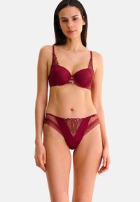 Soutien-gorge bourgogne avec armatures et dentelle, présentant un détail en cœur à l'avant. String en dentelle assorti avec un motif floral décoratif.