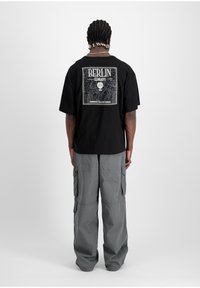 T-shirt en coton noir avec un grand graphique représentant une carte de Berlin en blanc au dos. Associé à un pantalon cargo gris comportant de nombreuses poches.