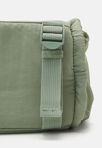 Zelená polstrovaná taška s texturovanou tkaninou, se sladěným popruhem a plastovou sponou pro bezpečné uzavření.