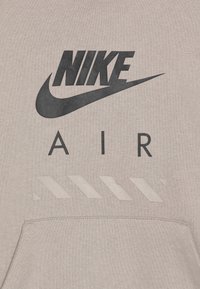 Šedá mikina s kapucňou s čiernym logom Nike, slovom "AIR" v čiernej farbe a horizontálnym vzorom nižšie v svetlejšej šedej. Mäkká, štruktúrovaná tkanina.