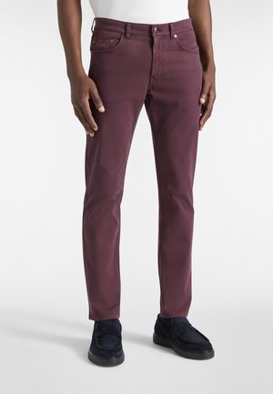 Pantalon slim-fit bordeaux en coton lisse, avec des passants de ceinture, des poches avant et une fermeture éclair. Associé à des mocassins bleu marine.