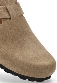 Zapato de ante color tostado con una textura suave y lisa, puntera redondeada y suela de goma negra. Presenta un sutil detalle de correa en la parte superior.