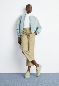 Veste bomber bleu clair, col roulé blanc, pantalon cropped beige, et baskets vert menthe. Tissus lisses, coupe décontractée, et détails de design minimalistes.