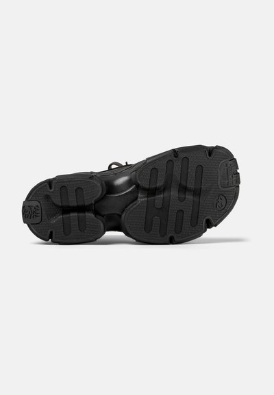 Sort sneakersål med tekstureret gummi, der har dybe riller og mønstrede greb for godt fodfæste. Minimalistisk design, ingen synlige logoer.