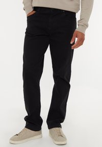 Pantaloni neri in cotone con taglio dritto e tasche laterali. Indossati con sneakers beige chiaro con un design testurizzato.