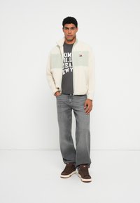 Herre fleecejakke i creme og mintgrøn, grå grafik t-shirt, grå jeans og brune sneakers med hvide såler. Lynlås lukning, krave, lommer.