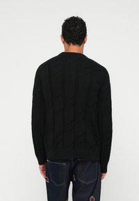 Schwarzer Pullover aus Kabelstrick mit einem strukturierten Design, rundem Halsausschnitt und gerippten Bündchen. Das Kleidungsstück hat eine lockere Passform und lange Ärmel.
