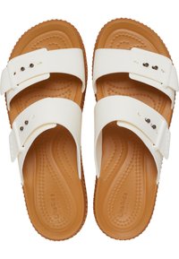 Witte slippers met twee verstelbare banden, een gestructureerde bruine binnenzool en een flexibele zool met een verhoogd stippenpatroon.