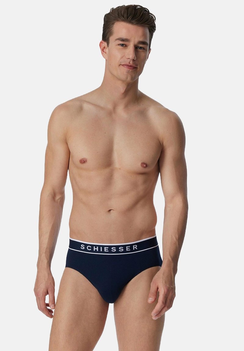 Slip navy blue con una vita bianca che presenta il marchio "SCHIESSER" in caratteri in grassetto. Realizzati in tessuto liscio e elastico.