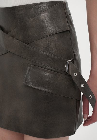 Kaki színű műbőr szoknya átlós panellel, slim fit fazonnal, oldalsó zsebbel és állítható hevederrel ezüst színű fémalkatrészekkel a derékpánton.