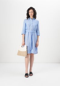 Light blue button-up dress with three-quarter sleeves and a tie belt, paired with a white and woven bag and black slide sandals.