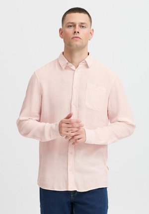 Camisa de botón de manga larga color rosa claro en una tela texturizada. Presenta un bolsillo en el pecho y un dobladillo recto, combinada con jeans de color azul oscuro.