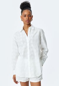 Hvid langærmet skjorte med knaplukning og et tekstureret bladmønster, parret med hvide shorts. Fremstillet af letvægtsstoffer med en afslappet pasform.