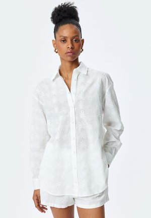 Hvid langærmet skjorte med knaplukning og et tekstureret bladmønster, parret med hvide shorts. Fremstillet af letvægtsstoffer med en afslappet pasform.