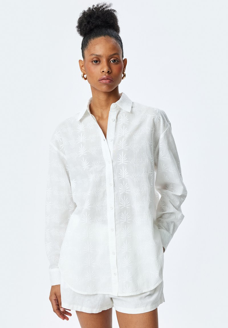 Hvid langærmet skjorte med knaplukning og et tekstureret bladmønster, parret med hvide shorts. Fremstillet af letvægtsstoffer med en afslappet pasform.