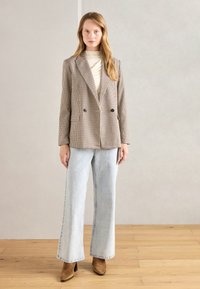 Bež in rjav houndstooth dvoredni blazer, kombiniran z svetlo modrimi širokimi jeans hlačami in rjavimi semiš škornji do gležnjev.