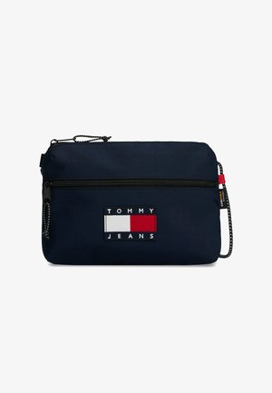 Pochette Tommy Jeans bleu marine avec poche zippée à l'avant, tirettes de fermeture éclair noires et écusson logo en rouge, blanc et bleu marine au centre avant.