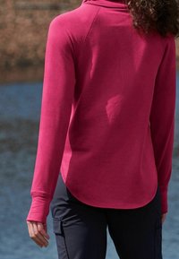 Maglietta a maniche lunghe con cappuccio di un colore magenta solido. Presenta un orlo arrotondato, un tessuto morbido, con polsini a coste e dettagli di cucitura.