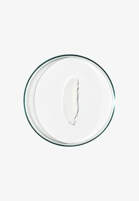 Witte crèmeswatch in een helder glazen petrischaaltje, gladde textuur, langwerpige vorm, op een witte achtergrond.