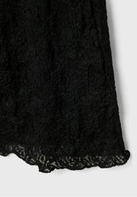 Tissu en dentelle noire avec un motif floral et un ourlet festonné sur un fond clair.