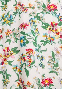 Tissu à motif floral crème, présentant des fleurs multicolores : rouge, bleu, jaune et rose, avec des feuilles vertes et des accents blancs.