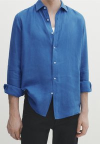 Blå linneskjorta med en avslappnad passform, knappad krage och uppvikta ärmar. Har en knappslå med vita knappar och en mjuk textur.