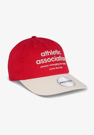Casquette de baseball rouge avec une visière crème. Présente un texte blanc indiquant "association athlétique" et un patch de logo circulaire sur la visière.