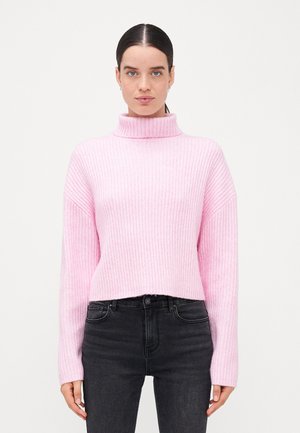 Pull en maille côtelée rose clair avec un col haut et des manches longues, présentant un design court. Porté avec un jean noir.