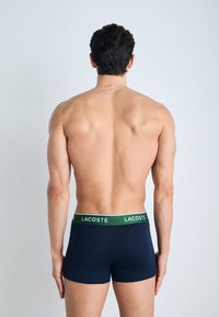 Boxers bleu marine avec une ceinture verte ornée du logo Lacoste. Le tissu est lisse et ajusté, présenté de dos.