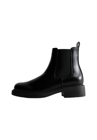 Botas de tobillo de cuero negro con paneles laterales elásticos, punta redondeada, tacón bajo y un detalle de borde cosido en la suela.